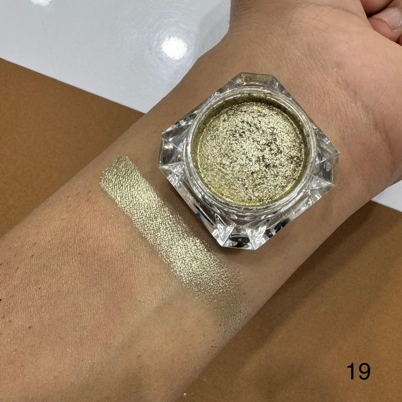Gold glitter makeup powder in a jar on a wrist with a swatch of color.