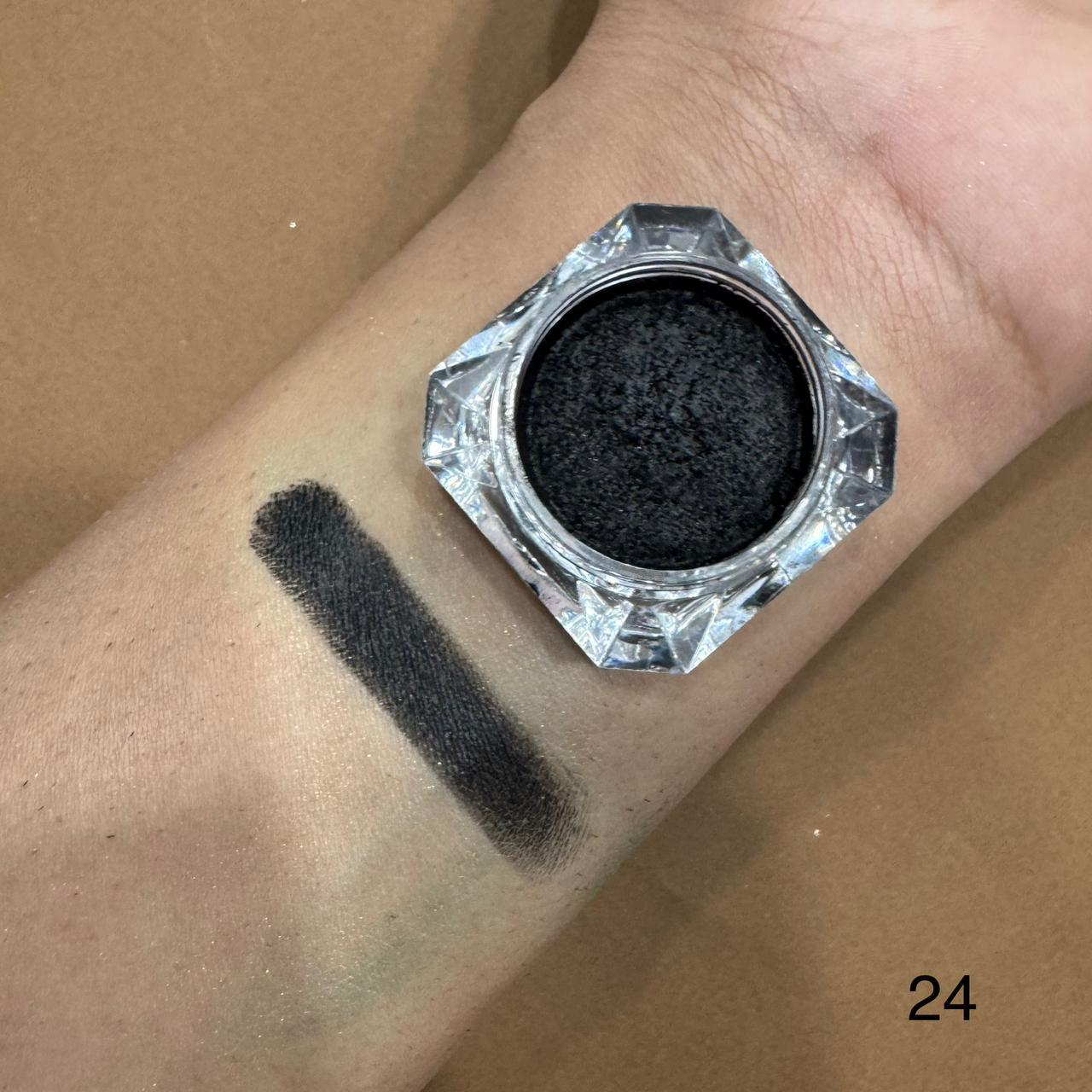Black eyeshadow jar with swatch on wrist against a brown background