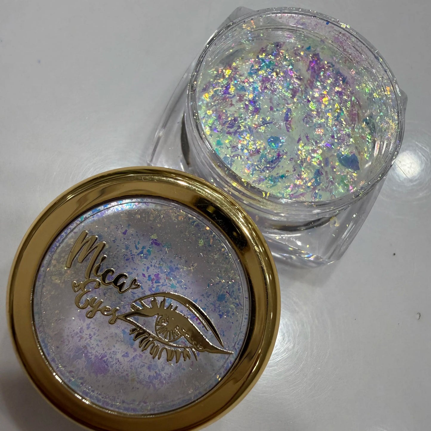 Glitter container with gold lid featuring an eye design and 'Micae' branding on a white background.